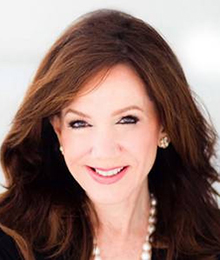 Laurie Silvers headshot, Caucasian businesswoman with brown hair is wearing a black blazer and pearl necklace, she's pictured in front of a white backdrop