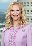 Melanie Griffin. Blonde female caucasian woman wearing a pink business coat. Tampa city skyline behind her in the background