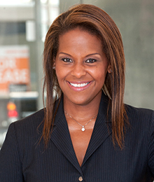 Michelle Delancy headshot, a smiling African American woman wearing a black suit, pictured in front of a window