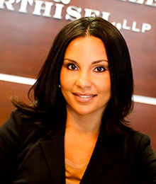 Niva Hiller-Harney is a young professional businesswoman wearing a black suit pictured in front of a brown wall