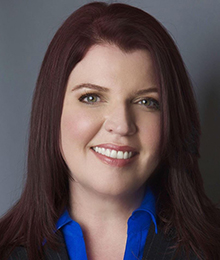 Renee Thompson headshot, Caucasian woman wearing business attire with a bright blue button down shirt, she has brown hair and is pictured in front of a solid gray backdrop
