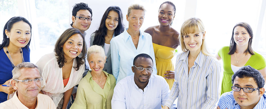 A diverse group of people casually pictured together, some standing and some are seated. Attire is business casual.