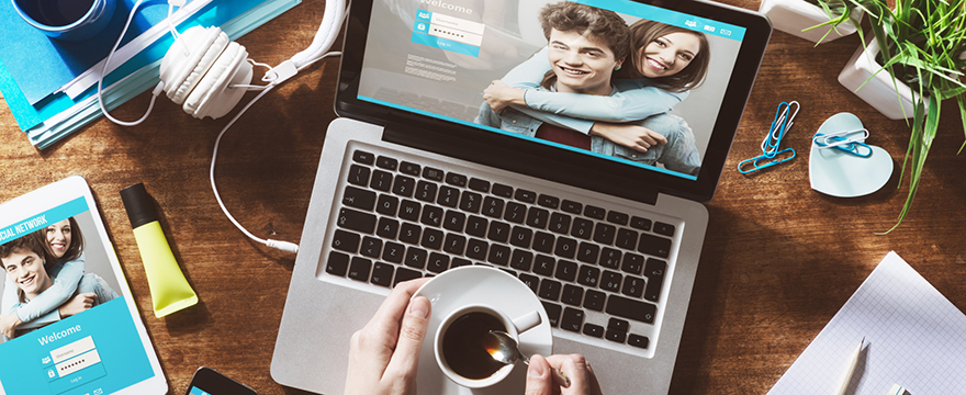 Close up of a laptop on a desk with hands resting on keyboard, holding a cup of coffee