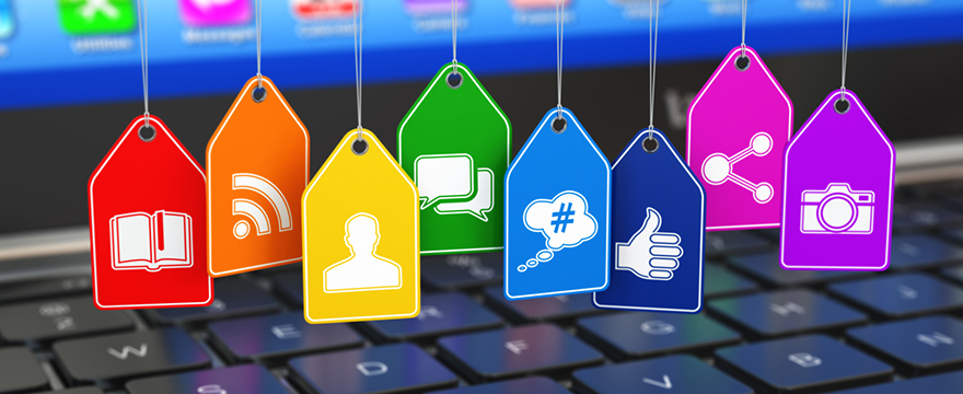 A series of social icons, each pictured on a different colored hang tag, all hanging in a row above a keyboard