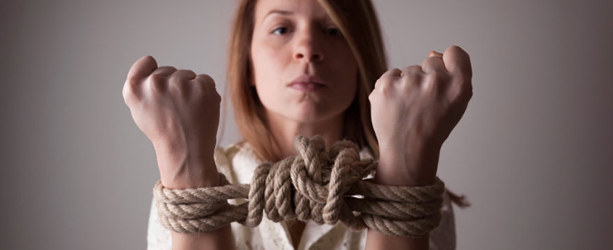 Somber looking, middle aged, Caucasian woman is holding up both hands to show they are tied together with thick ropes and a large knot