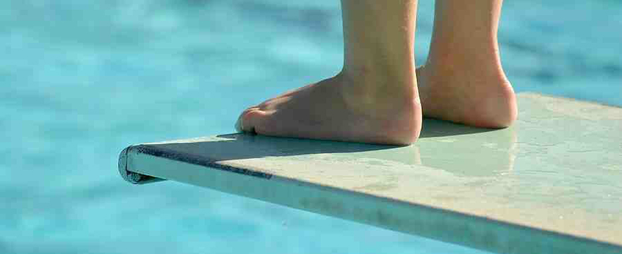 Close up image of feel standing on a diving board, over a swimming pool
