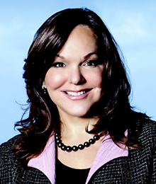 Hilarie Bass headshot, Caucasian female with dark hair wearing a lilac blouse with a black blazer and a black beaded necklace