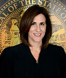 Honorable Lisa Walsh headshot, Caucasian female with short dark brown hair is pictured in front of a government seal
