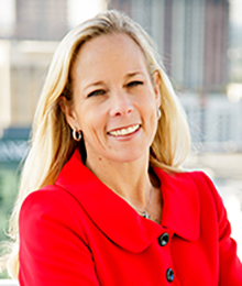 Jamie Billote Moses headshot, Caucasian business woman with blonde hair is pictured outside smiling, wearing a red business jacket