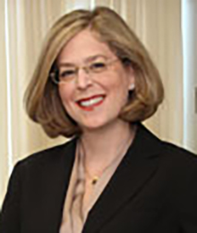 Julie Braman Kane headshot, Caucasian businesswoman is smiling, wearing a black suit and glasses