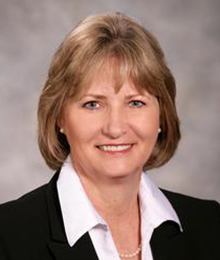 Kelly Sullivan headshot, Caucasian business woman with sandy blonde hair is wearing an black suit with a white button down shirt