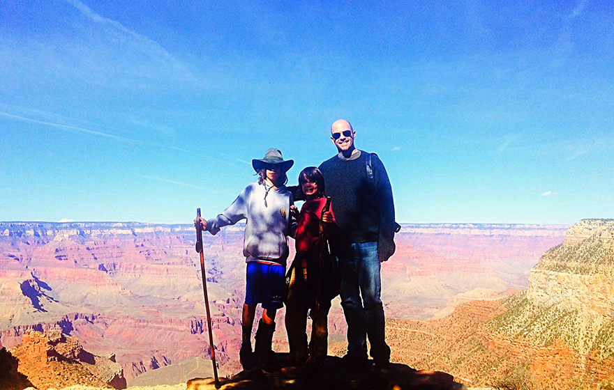 A group of 3 people are standing at the rim of a majestic canyon on a beautiful sunny day