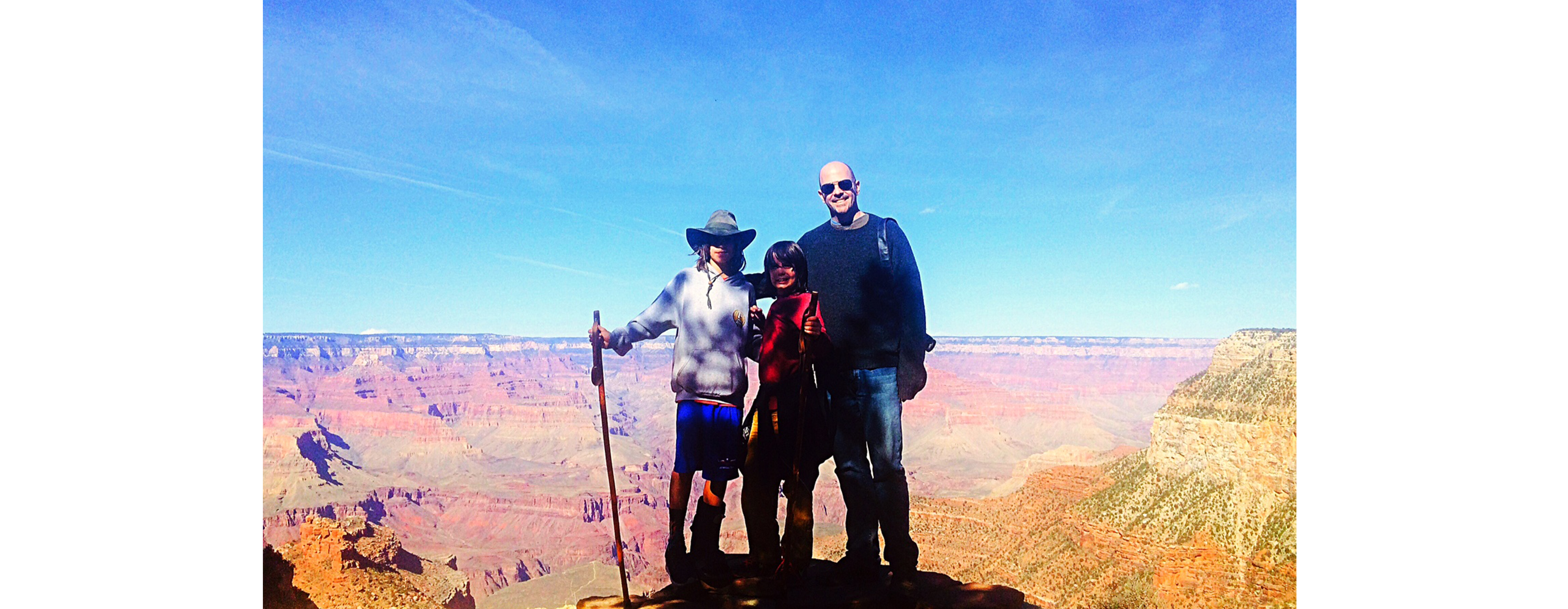 A group of 3 people are standing at the rim of a majestic canyon on a beautiful sunny day