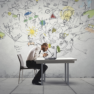 Businessman seated at a desk with a laptop, behind him the wall is covered with creative and colorful graffiti
