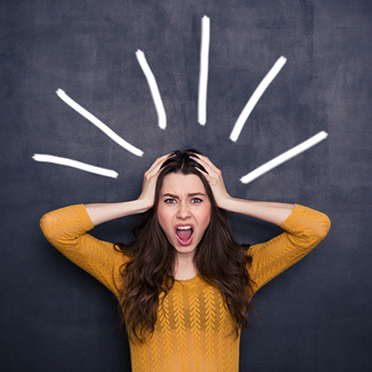 Young woman appears stressed, hands on her head, yellow sweater, chalkboard background