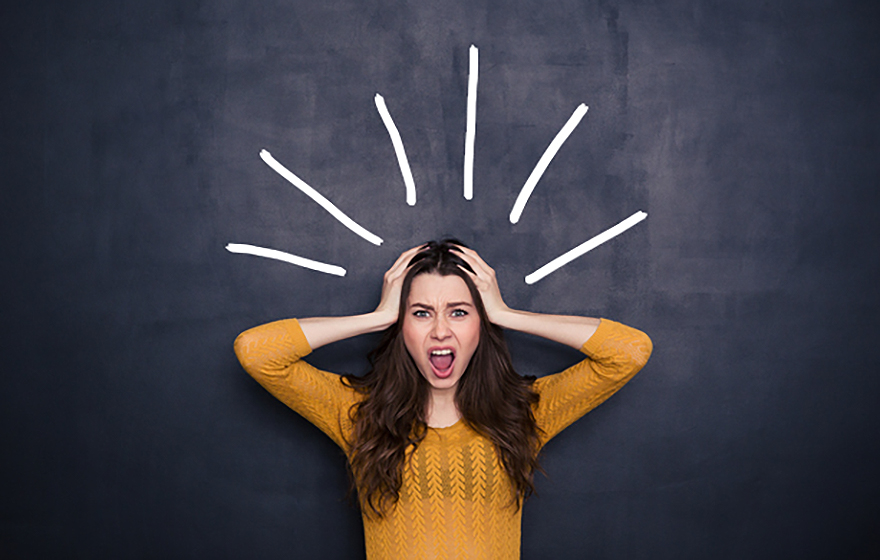 Young woman appears stressed, hands on her head, yellow sweater, chalkboard background