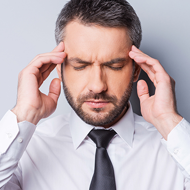 Stressed businessman has his hands on his temples, eyes closed, standing in front of a gray background