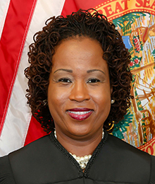Nirlaine Tallandier Smartt headshot, African American woman with short, dark hair, pictured in front of an American flag