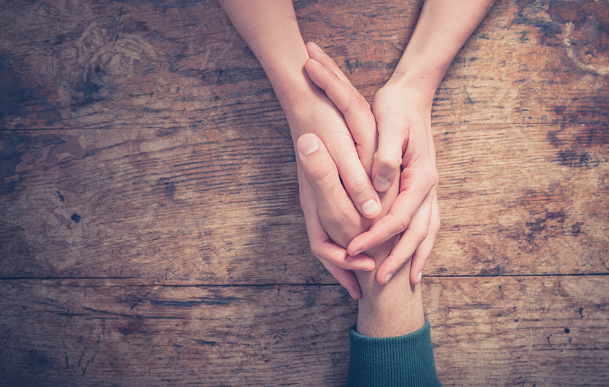 Close up on a man and a woman holding hands at a wooden table
