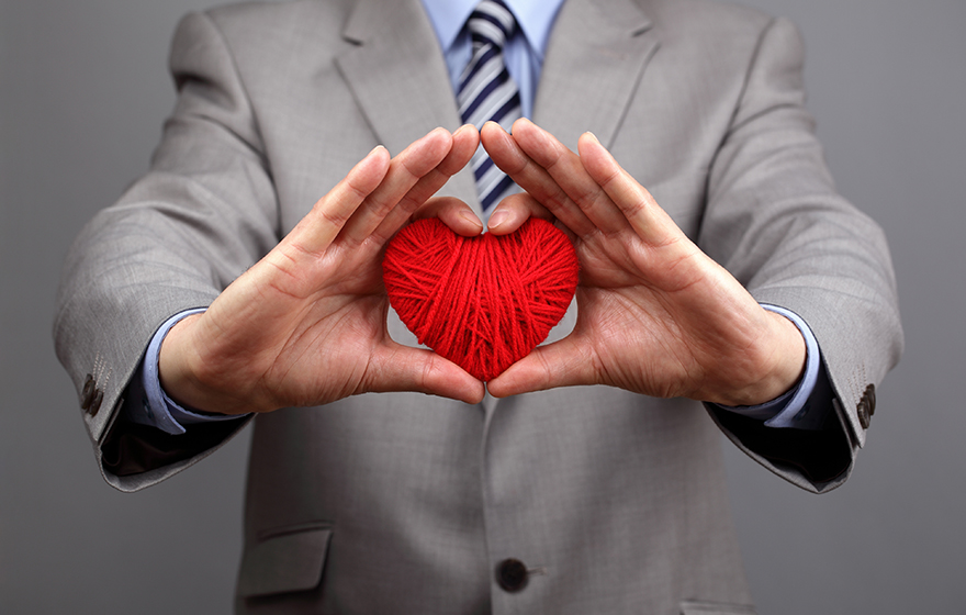 Attorney dressed suit, holding up a yarn heart. Showing heart/love for doing pro bono work.