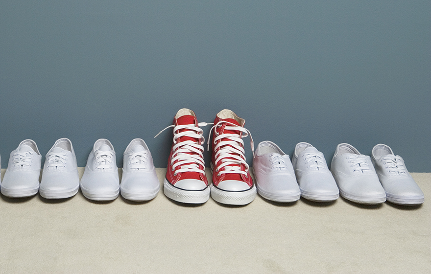 Pair of shoes in row against wall, all white except for one red pair in the middle