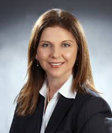 Caucasian female lawyer with light brown hair, wearing a dark black suite and white collared shirt.
