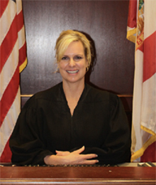 HonorableLeahCase_220x260 Honorable female judge seated at the bench with a flag on each side of her