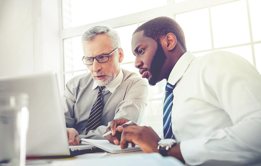 Photo of mature Caucasian lawyer and his younger African American male, colleague looking at a laptop together.