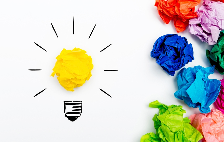 Crumpled paper light bulb over white background, surrounded by crumpled colorful paper. Idea concept.