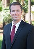 Zack Zuroweste a young Caucasian man in a black suit with a red tie with sunny palm trees in the background