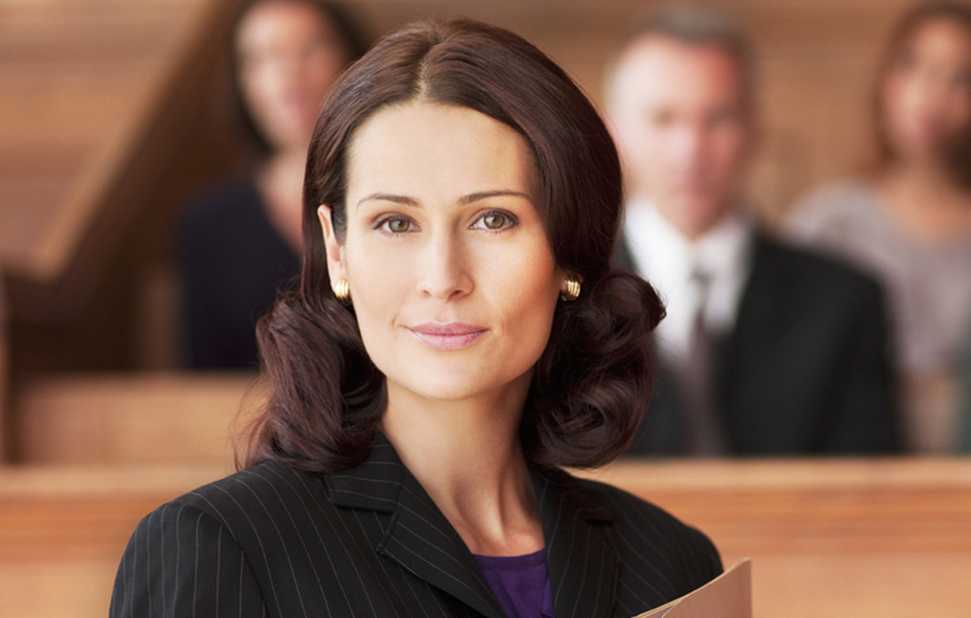 Smiling Caucasian brunetter female lawyer holding file in courtroom with a jury behind her