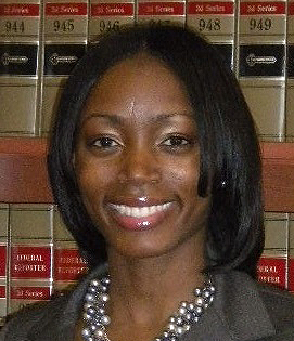 Keshara Davis headshot of a young smiling African American woman, she has medium length black has and is wearing a dark grey blazer and a pearl statement necklace