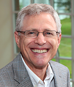 Larry Krieger for the College of Law headshot of an older smiling Caucasian man with grey hair wearing glasses, a grey striped sportcoat and a white shirt