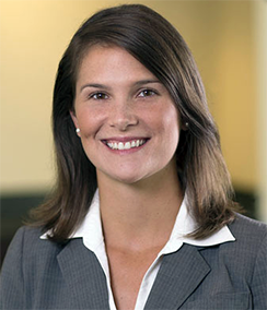 Lauren Purdy headshot of a young Caucasian woman with medium length brown hair wearing a grey blazer, white shirt and simple pearl earrings
