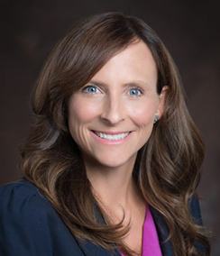Margaret Good headshot of a middle aged smiling Caucasian woman with brown hair and blue eyes wearing a pink blouse and a navy blue blazer