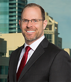 Ron Ponzoli a Caucasian man with glasses, brown hair and a beard in front of cityscape