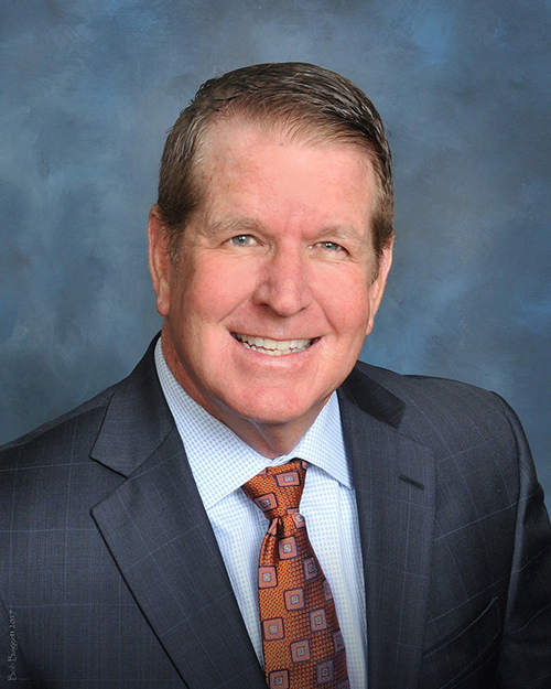Thomas R. Bopp headshot of a cheerful smiling middle aged Caucasian man in a dark blue suit with a light colored shirt and a maroon tie.