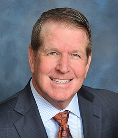 Thomas R. Bopp headshot of a cheerful smiling middle aged Caucasian man in a dark blue suit with a light colored shirt and a maroon tie.