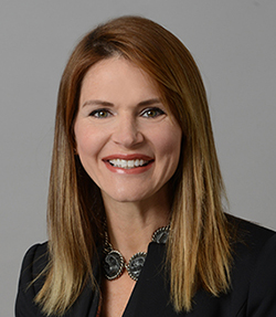 Deborah Baker-Egozi headshot of a happy Caucasian woman with light brown hair. She is smiling and is wearing pink lipstick. She has brown eyes and is wearing a large coin necklace and a black blazer.