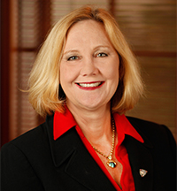 Julia Frey headshot of a Caucasian woman with medium length blonde hair wearing a bright red shirt, black blazer and a heart necklace. She has a warm happy smile and is wearing red lipstick.