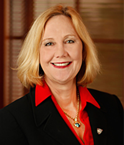 Julia Frey headshot of a Caucasian woman with medium length blonde hair wearing a bright red shirt, black blazer and a heart necklace. She has a warm happy smile and is wearing red lipstick.