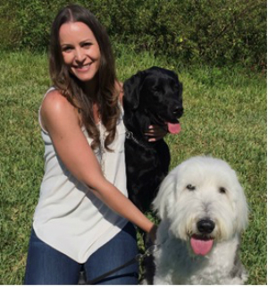 Rebecca Kibbe photo Rebecca Kibbe a young Caucasian woman in a white tank top and jeans with two dogs and grass in the background.