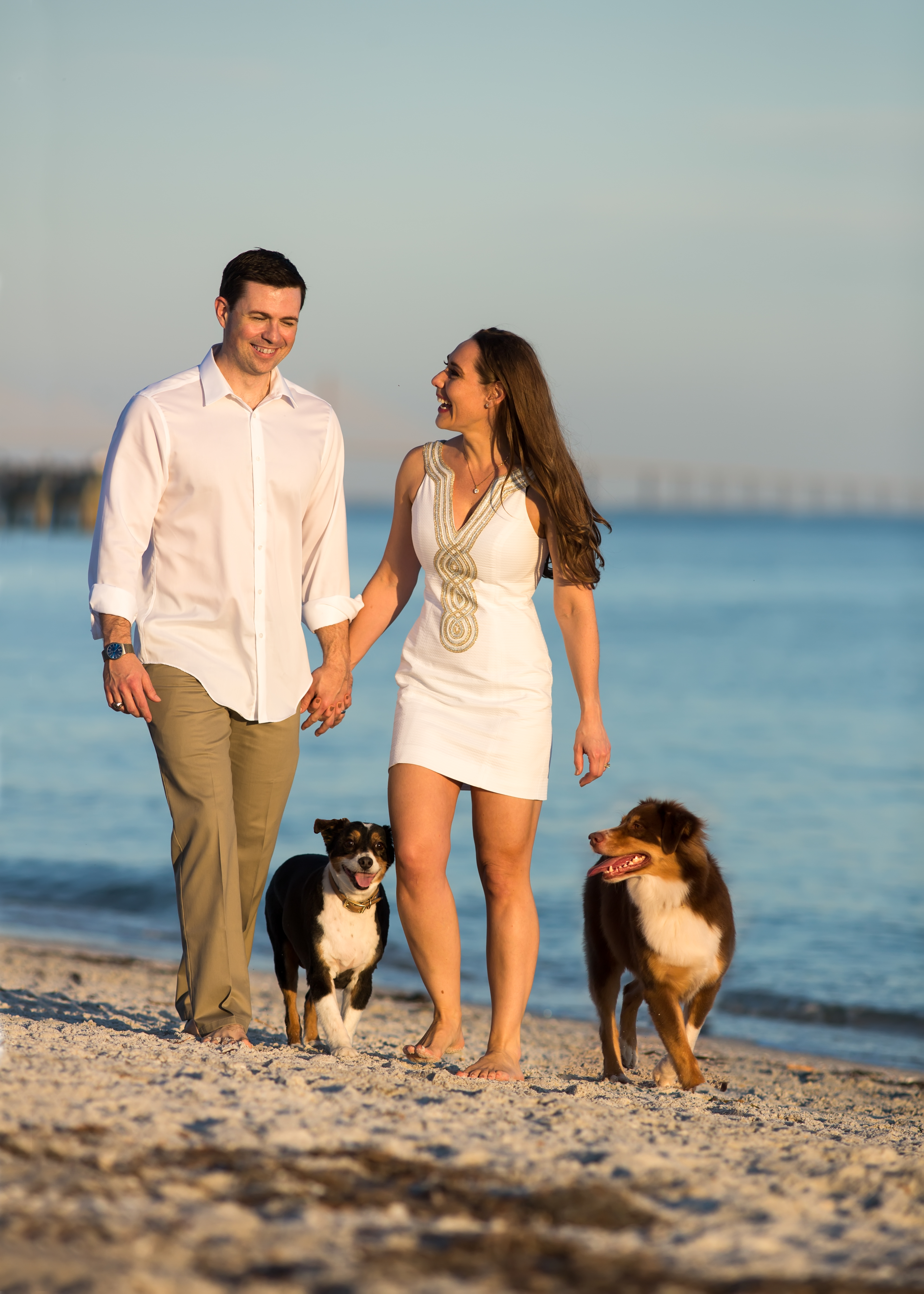 Stephanie Hayes photo Stephanie Hayes a Caucasian woman with long brown hair with male significant other who is Caucasian and two black white and brown dogs. They are on the beach and both people are wearing white.