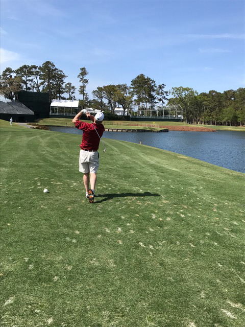 Thomas R. Bopp teeing off on golf course he is a Caucasian man wearing a red collared shirt, tan khaki shorts and a white hat.