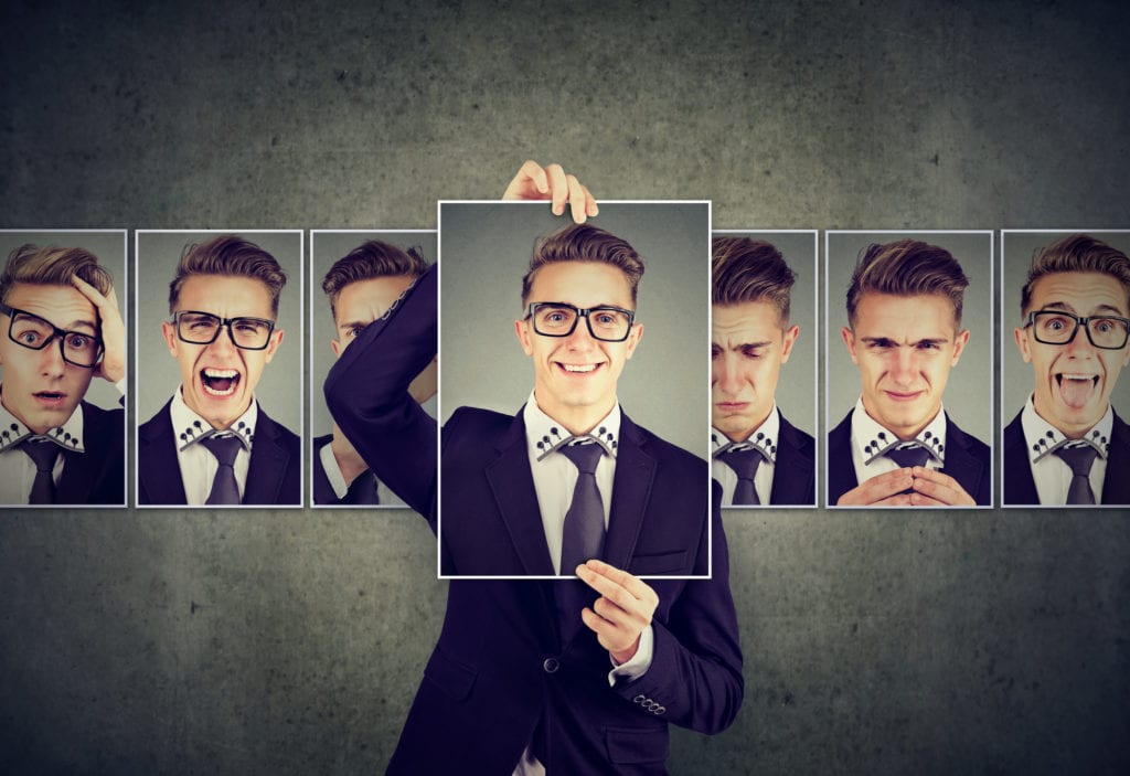 Positive masked Caucasian man in suit and glasses expressing different emotions by holding a large image over his face