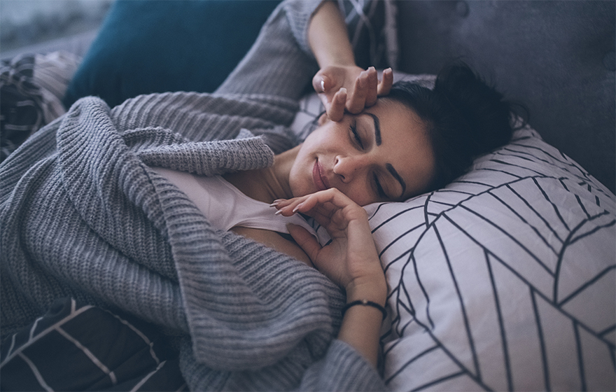 Young Caucasian woman with black hair and black eyebrows waking up at her own bed alone, with a smile