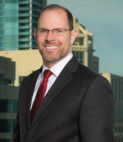 Ron Ponzoli a Caucasian man with glasses, brown hair and a beard in front of cityscape