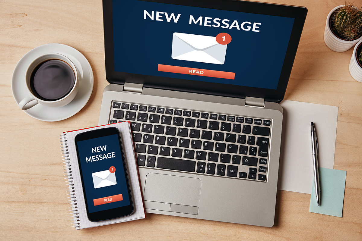 New message notification concept on laptop and smartphone screen over wooden table. All screen content is designed by me. Flat lay