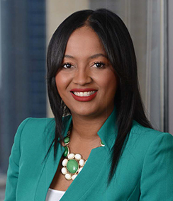 Alison Smith headshot African American woman in a teal blazer and white shirt in front of office window, she is smiling and wearing lipstick, and has long black hair.