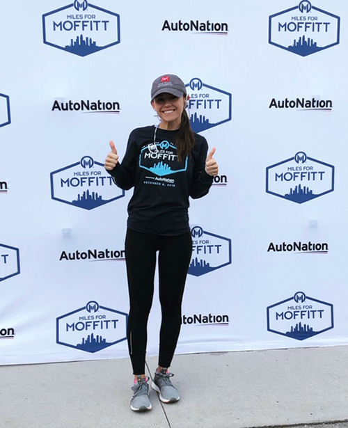 Melina Garcia, a young Latina woman in a grey hat, sneakers and running gear standing in front of event backdrop